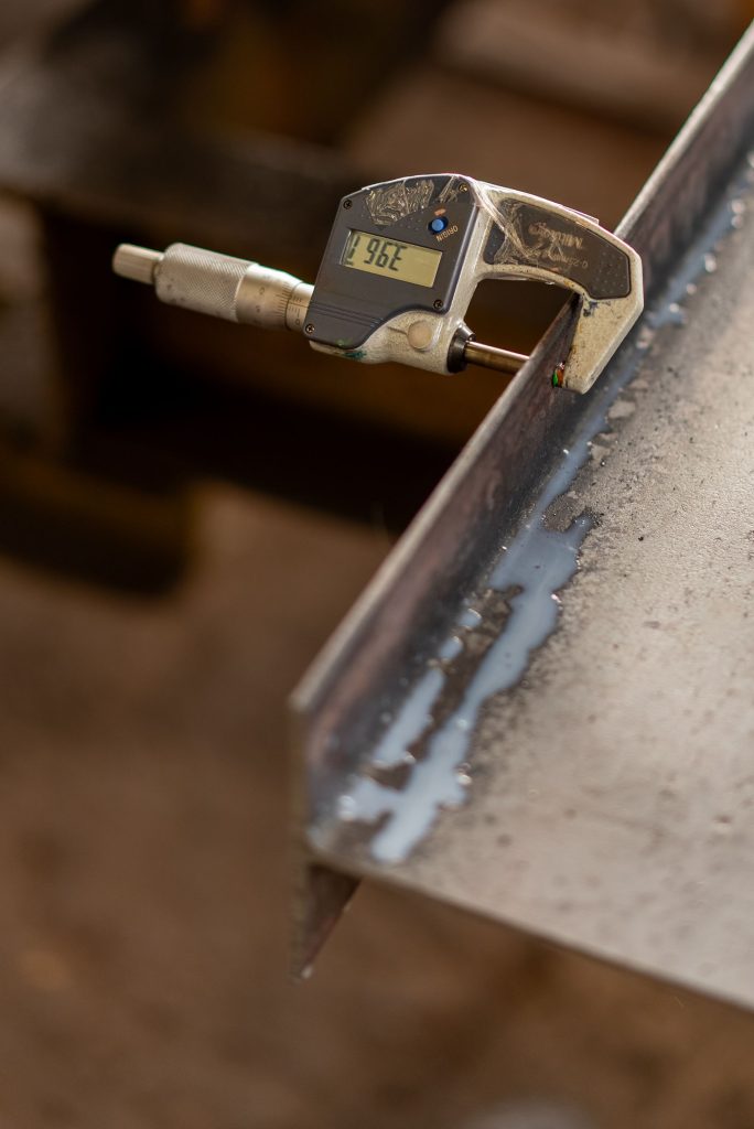 Close-up of a digital micrometer measuring the thickness of a metal sheet, showcasing industrial precision. Gros plan d'un micromètre numérique mesurant l'épaisseur d'une feuille de métal, mettant en avant la précision industrielle.
