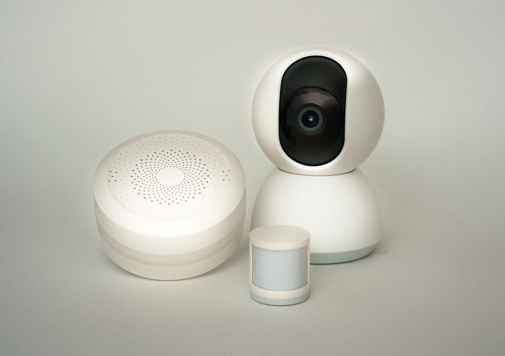 Modern smart home devices including a camera and sensors on a neutral background. Appareils domotiques modernes incluant une caméra et des capteurs sur un fond neutre.