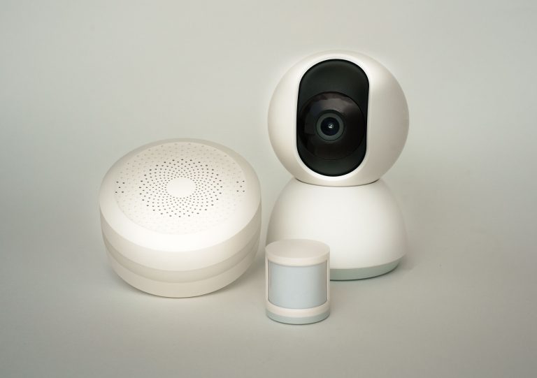 Modern smart home devices including a camera and sensors on a neutral background. Appareils domotiques modernes incluant une caméra et des capteurs sur un fond neutre.